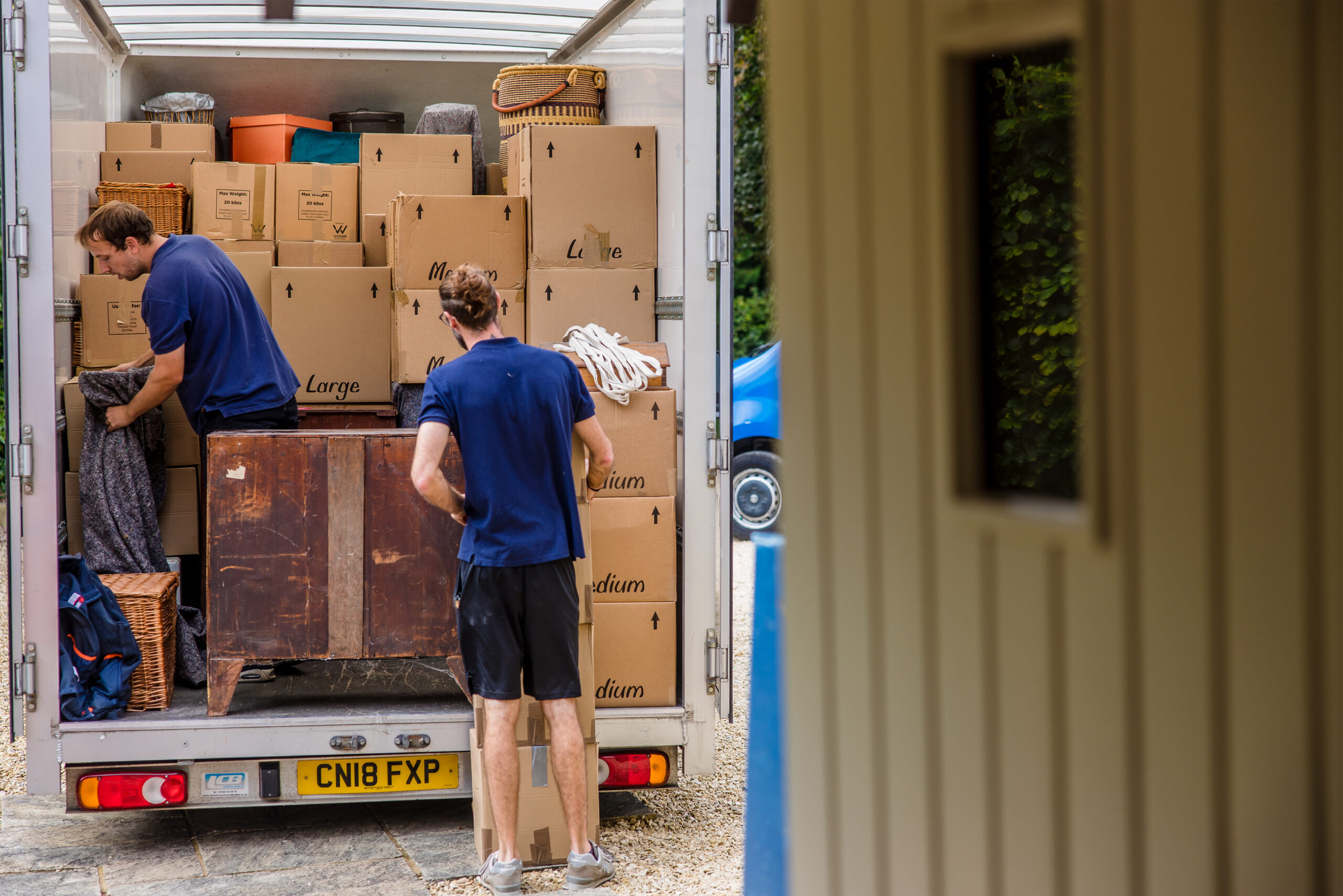 Two mean loading boxes and furniture onto the back of a removal van outside.