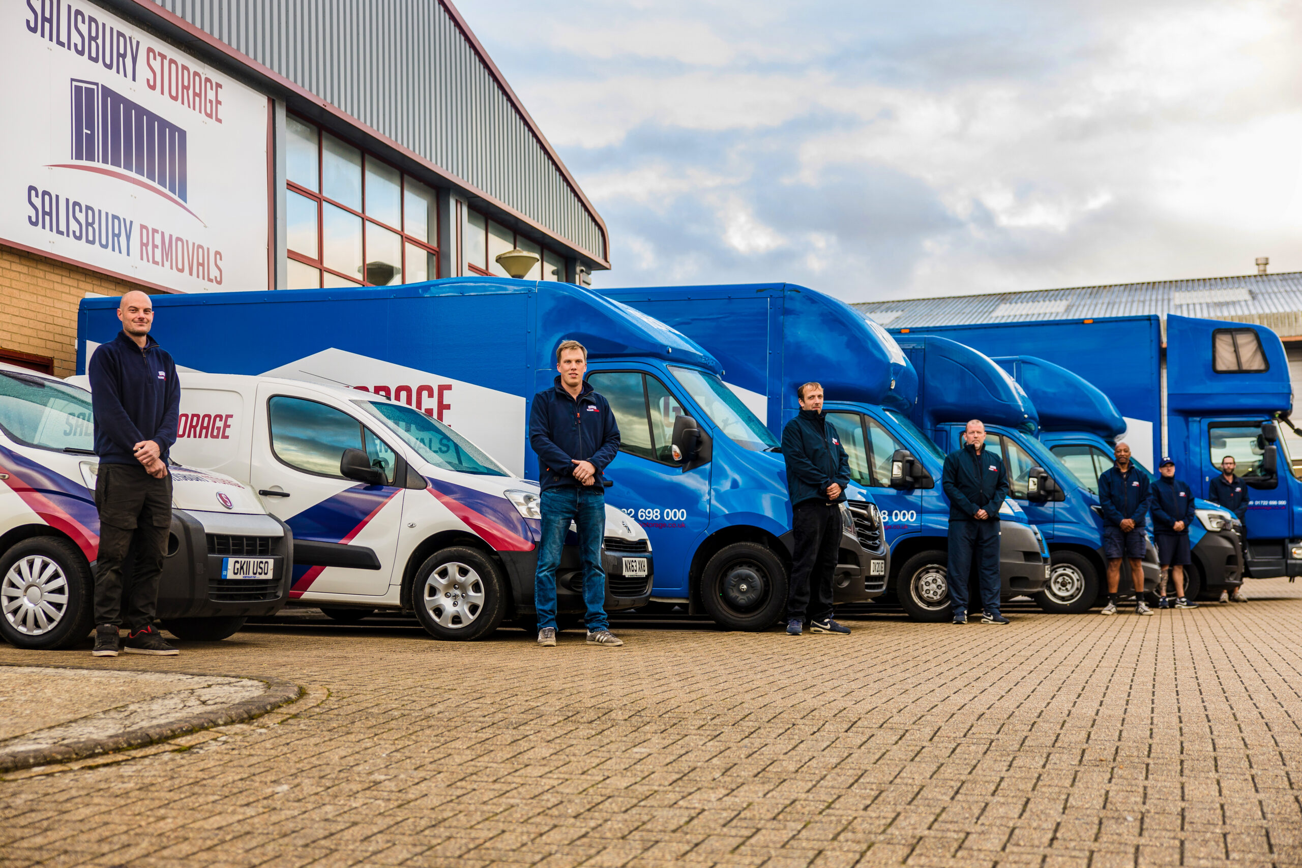 A group of men standing in front of blue vans and lorries, ready for a removal and storage journey.