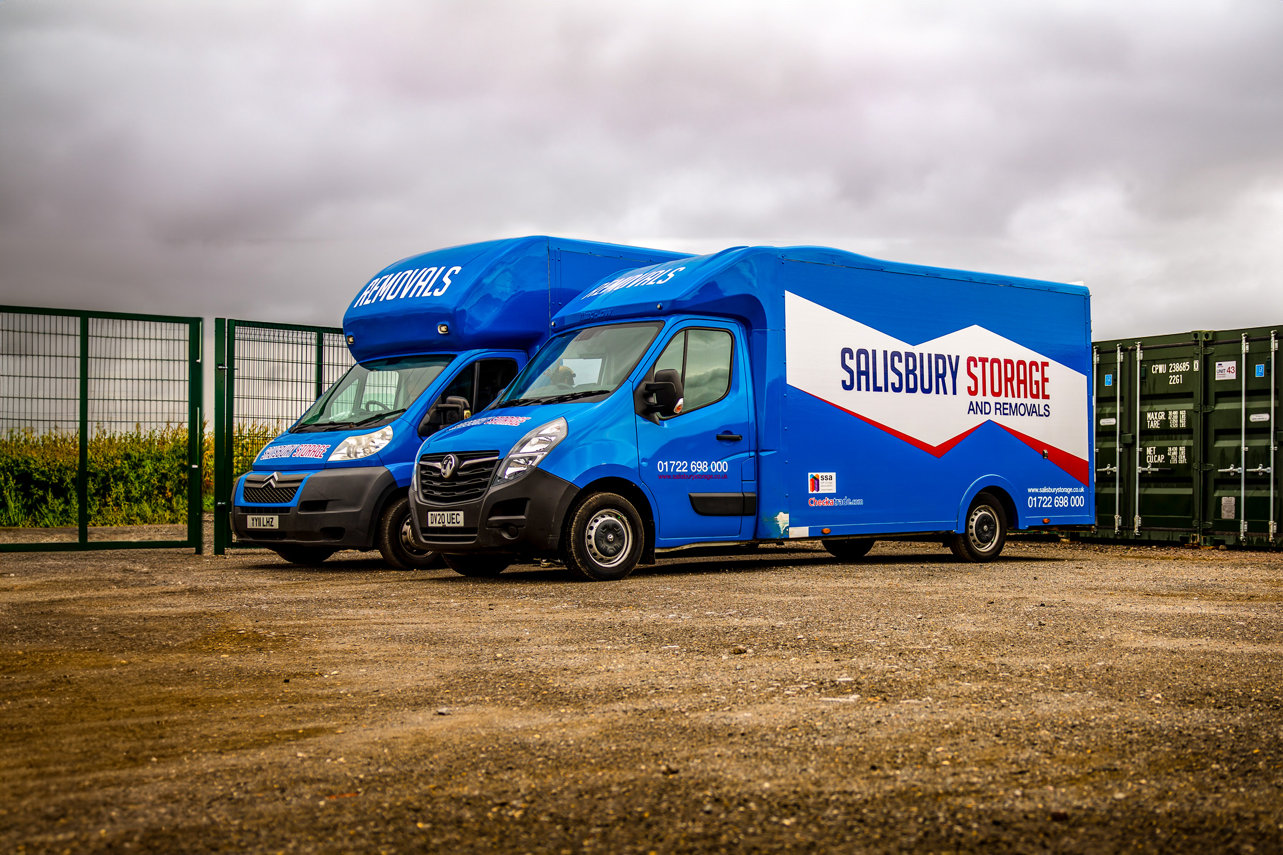 Two blue vans with the Salisbury storage and removals logo parked side by side in front of large storage containers.