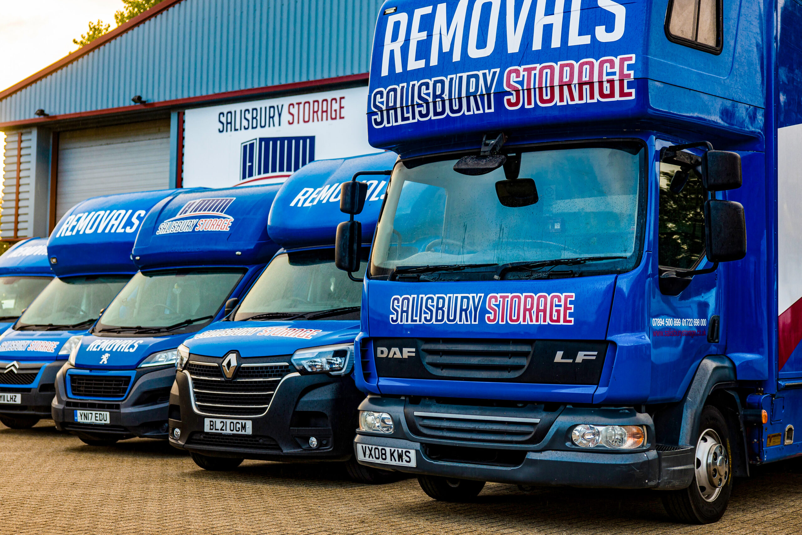 A fleet of parked blue vans and lorries outside a building, showcasing a harmonious blend of colours and a strong industrial presence.
