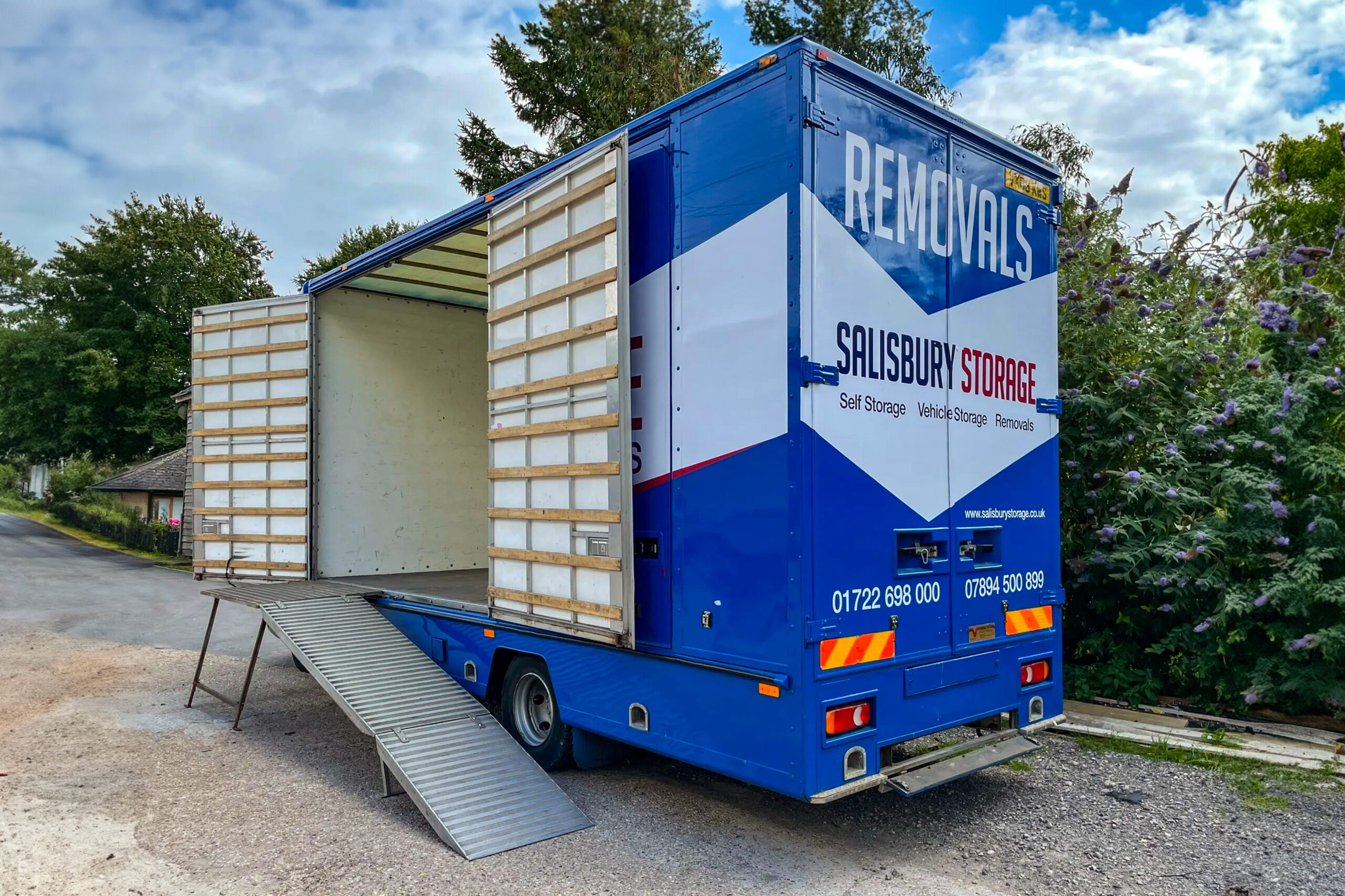 A large blue storage and removal lorry with a ramp attached and side doors opened, ready to transport belongings efficiently.