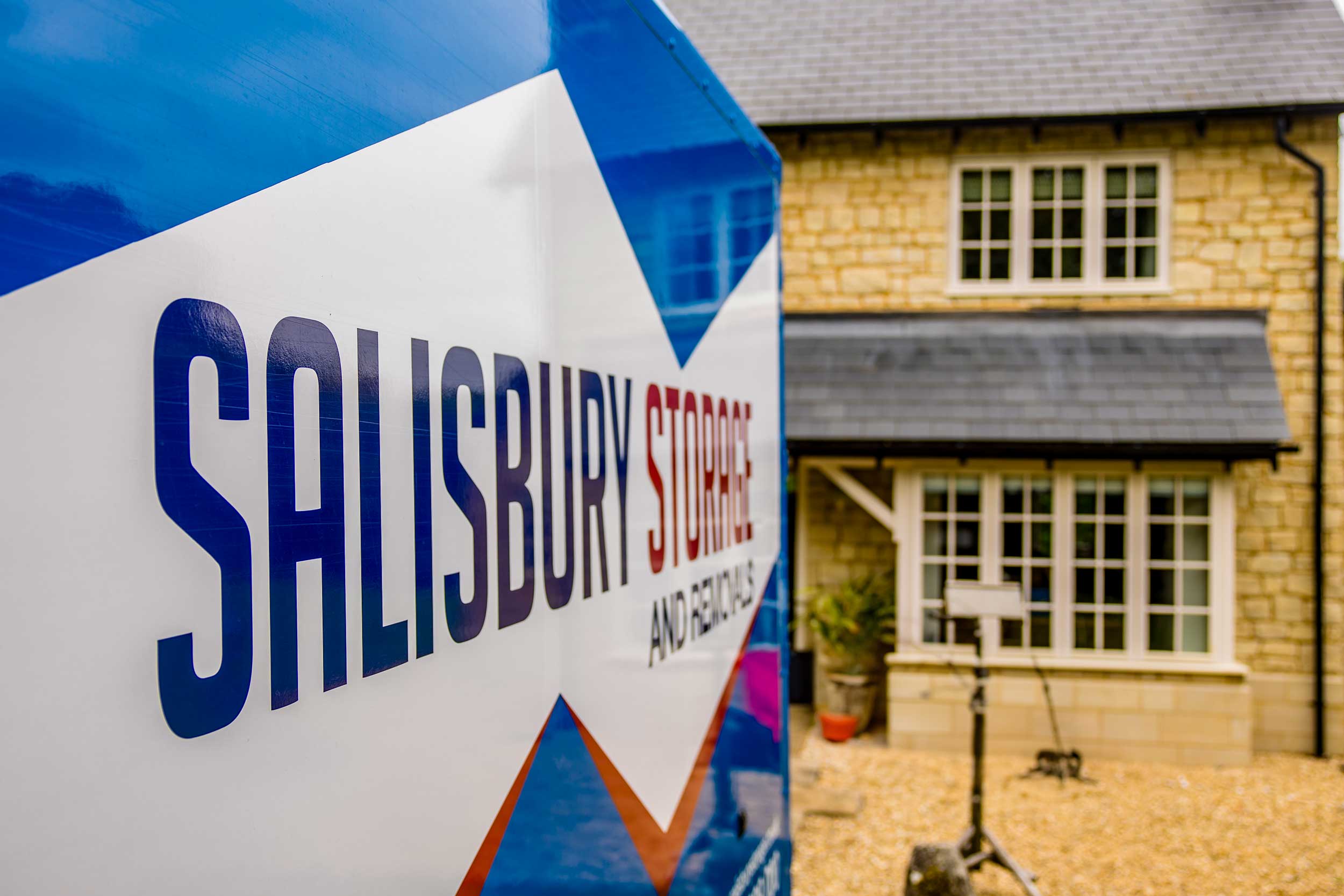 Close up of the logo on the side of a salisbury storage and removals van with a residential property in the background.