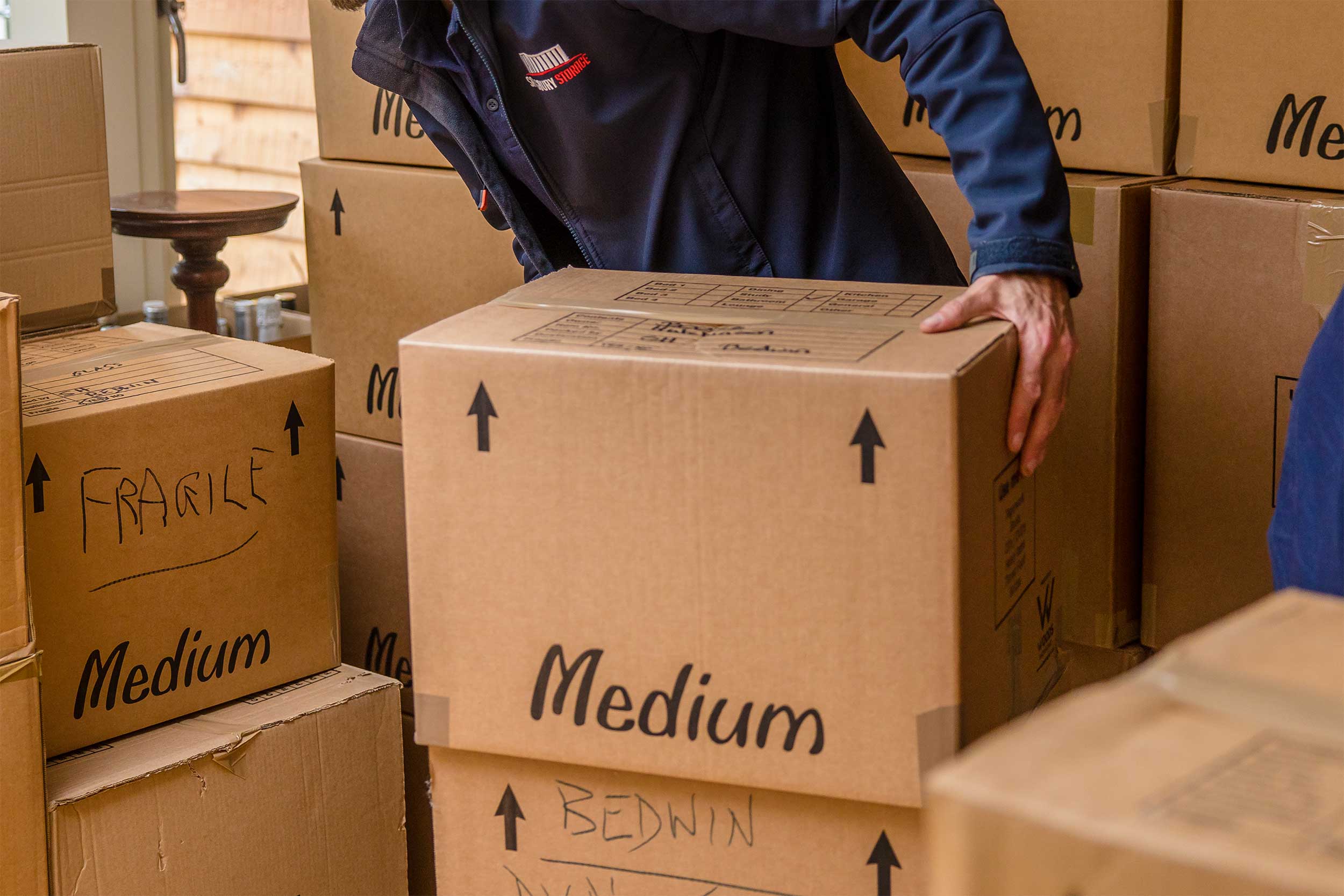 A removals man diligently relocates boxes within a room, displaying efficiency and organisation in his task.