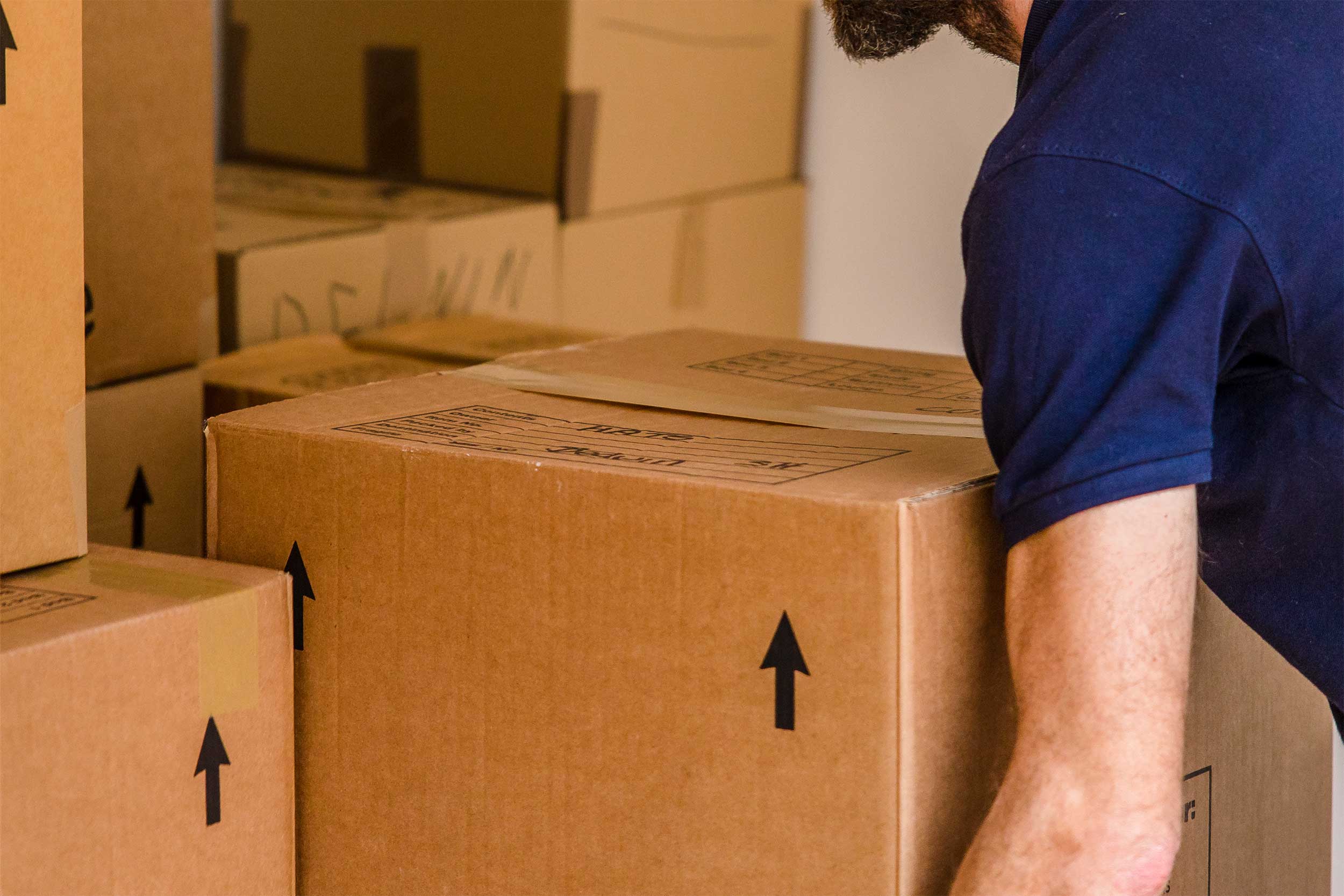 A removals and storage man diligently relocates boxes within a room, making sure they are stacked safely.