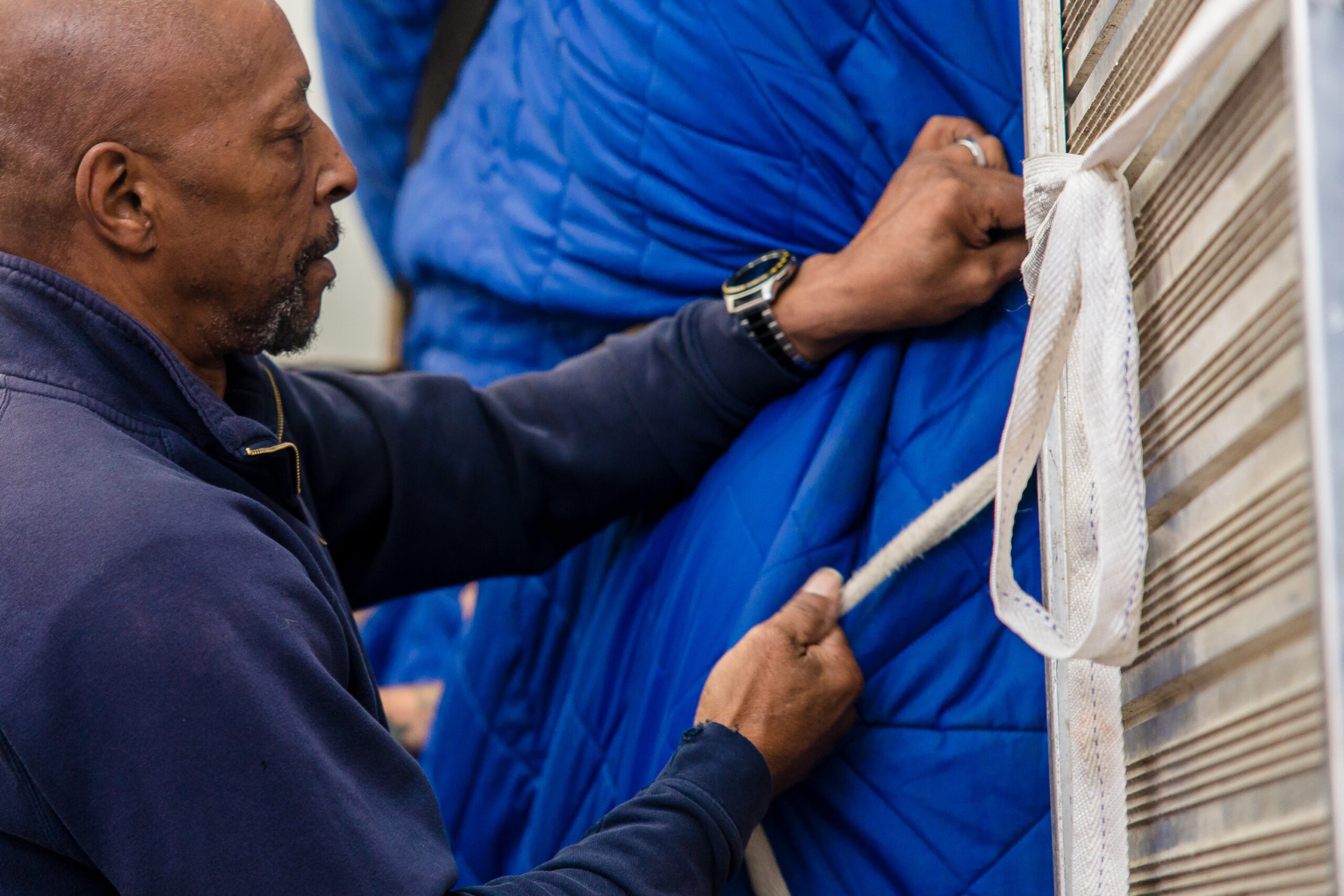 A removals and storage man secures a unique item within the back of the van covered in a blue blanket.