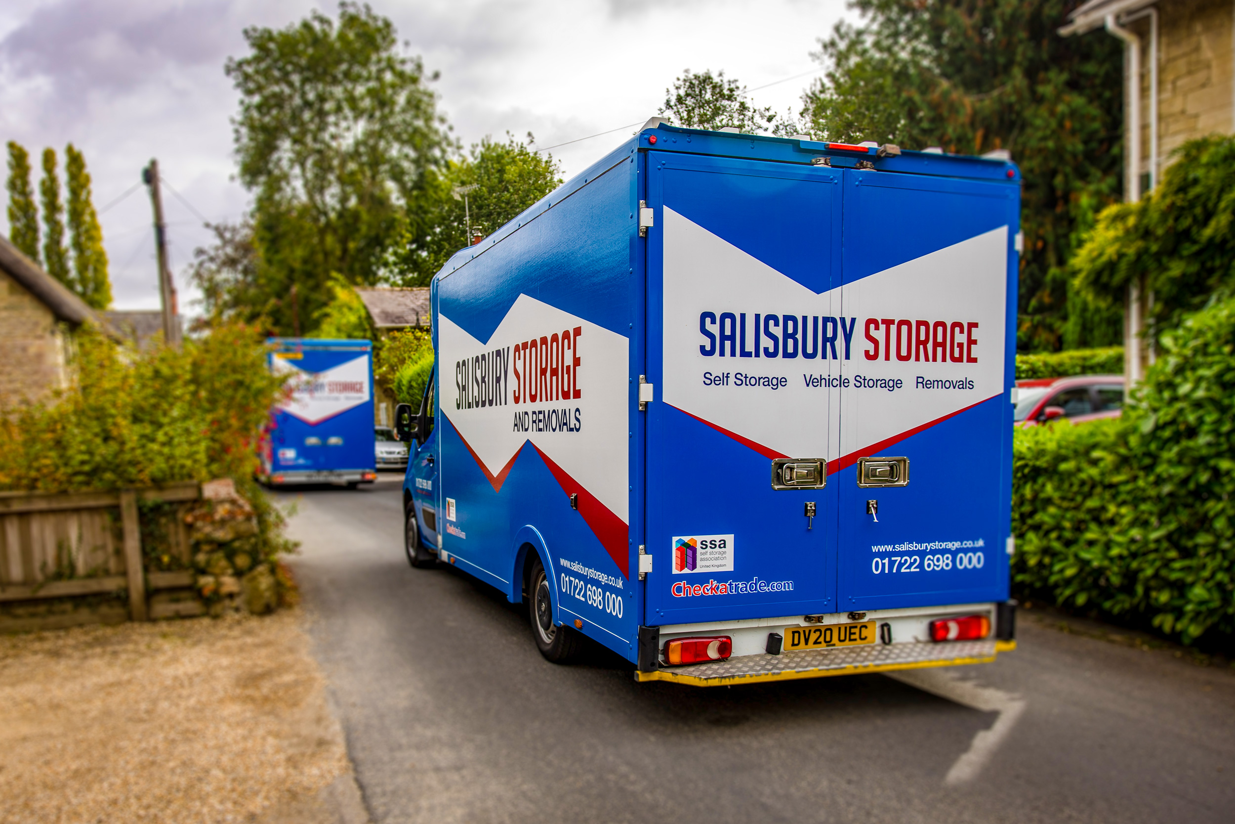 Two removals and storage vans driving down a scenic road on a journey transporting belongings.