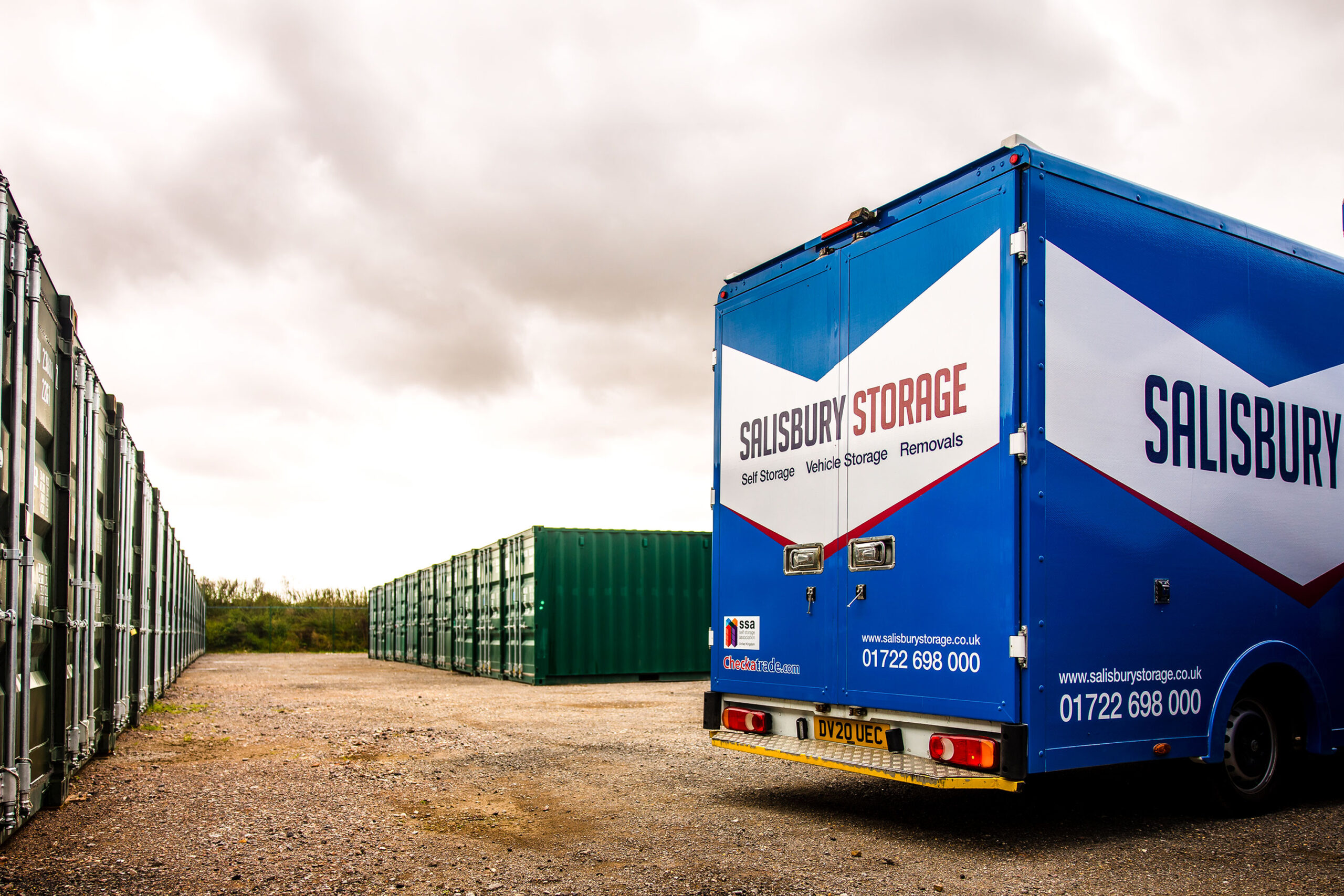 A blue removals and storage lorry, parked in the middle of dark green storage containers.